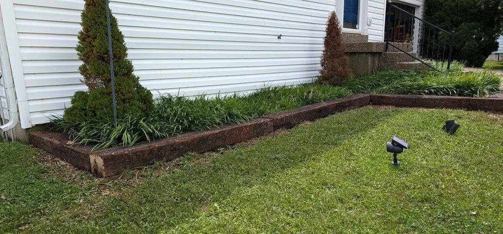 The same border rebuilt with straight railroad-tie edging holding a clean, level bed against the house wall.